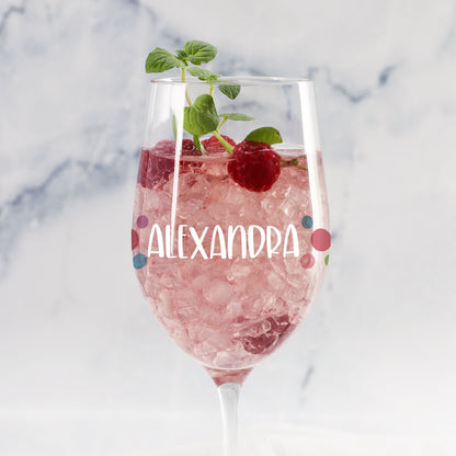 Personalisiertes Weinglas mit bunten Punkten und Name „Alexandra“, gefüllt mit rosa Getränk, Eis, Himbeere und Minze