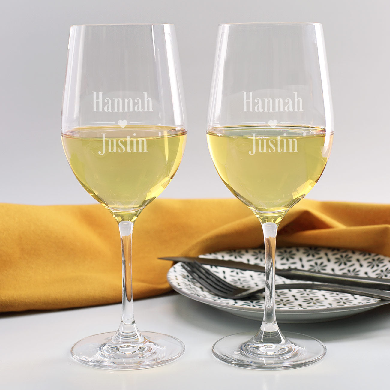 Zwei Weißweingläser mit Gravur der Namen Hannah und Justin, Herzmotiv zwischen den Namen