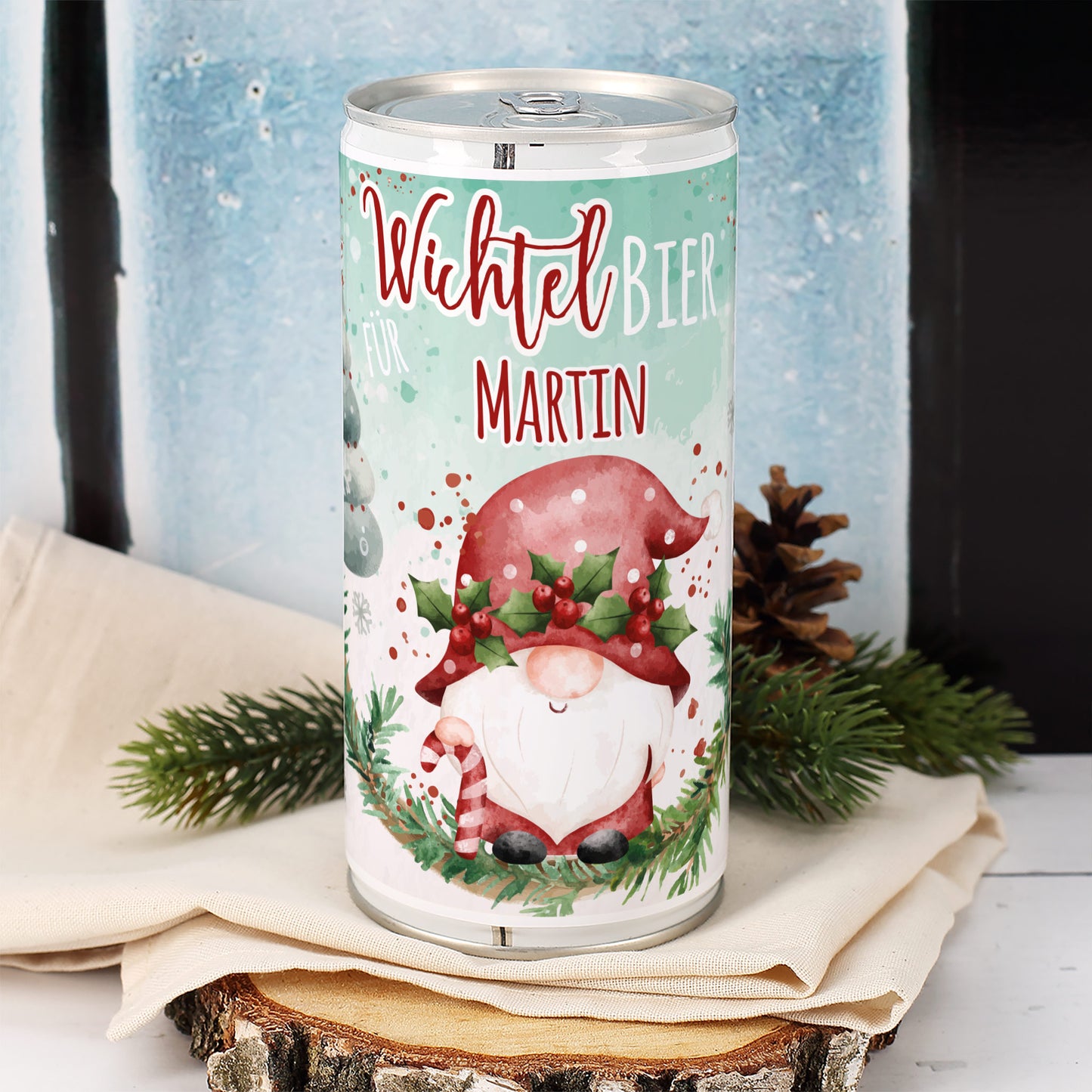 Personalisierte Bierdose mit Wichtelmotiv und Name Martin vor winterlichem Fenster, dekoriert mit Tannenzweig und Zapfen.