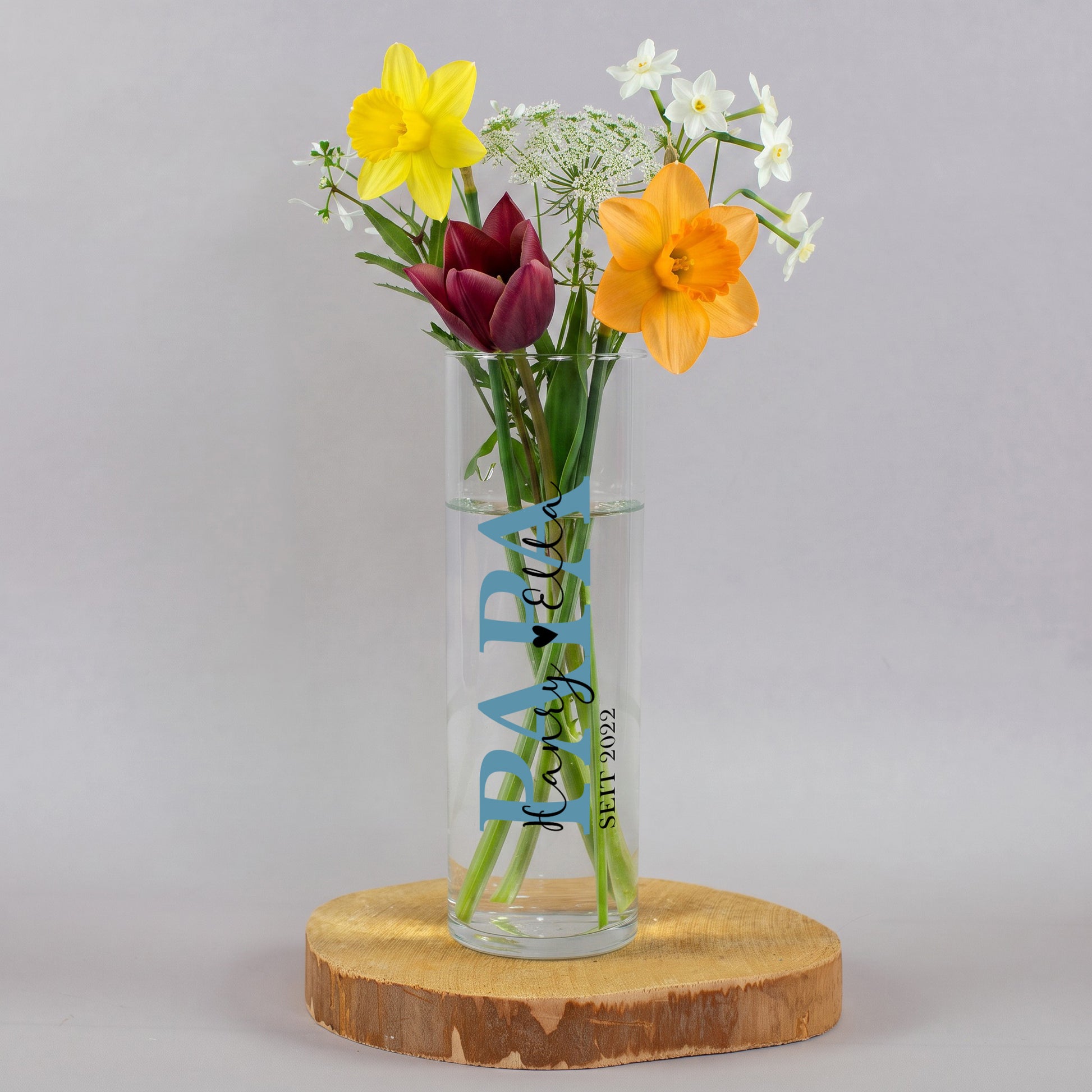 Schmale Glasvase für Papa mit Wunschtext, Herzsymbol und Jahreszahl 2010, gefüllt mit bunten Blumen und als dekoratives Geschenk arrangiert