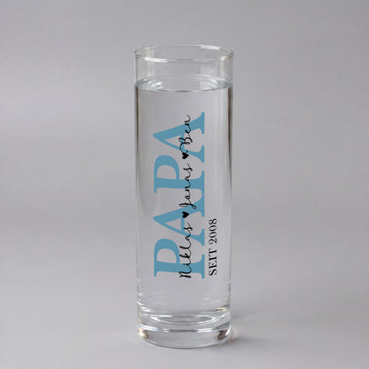 Personalisierte Papa Vase aus Glas mit blauem Schriftzug, Name und Jahreszahl 2022, dekoriert mit Frühlingsblumen auf Holzscheibe