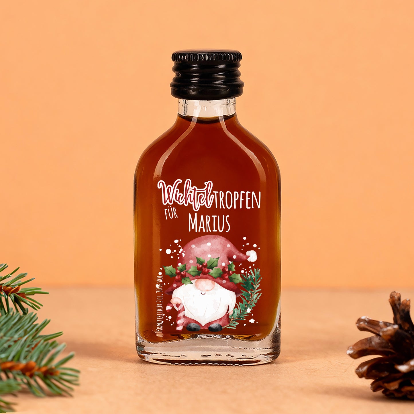 Wichteltropfen-Flasche mit dunklem Kräuterlikör, personalisiert mit Name, weihnachtliche Deko im Hintergrund.