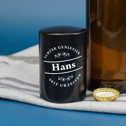 Schwarzer Push-Up Flaschenöffner mit Genießer-Spruch auf dunklem Untergrund