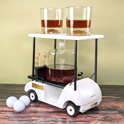 Golfcart-Whiskyset mit befüllten Gläsern und Karaffe auf dunklem Holz mit Golfbällen