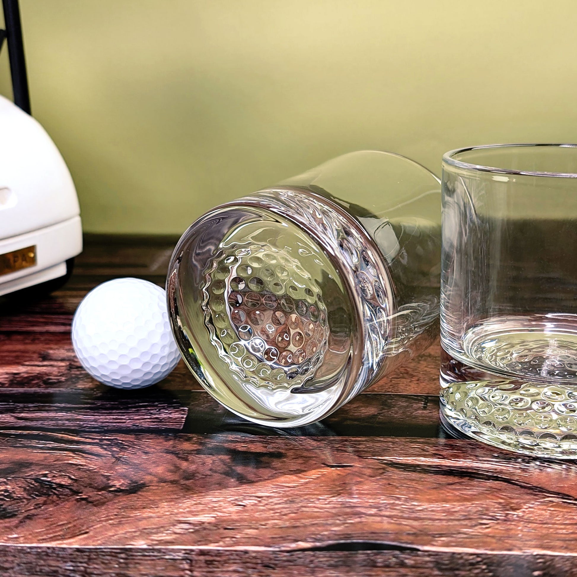 Zwei Gläser mit Golfstruktur liegend auf Holzboden neben dem Golfcart