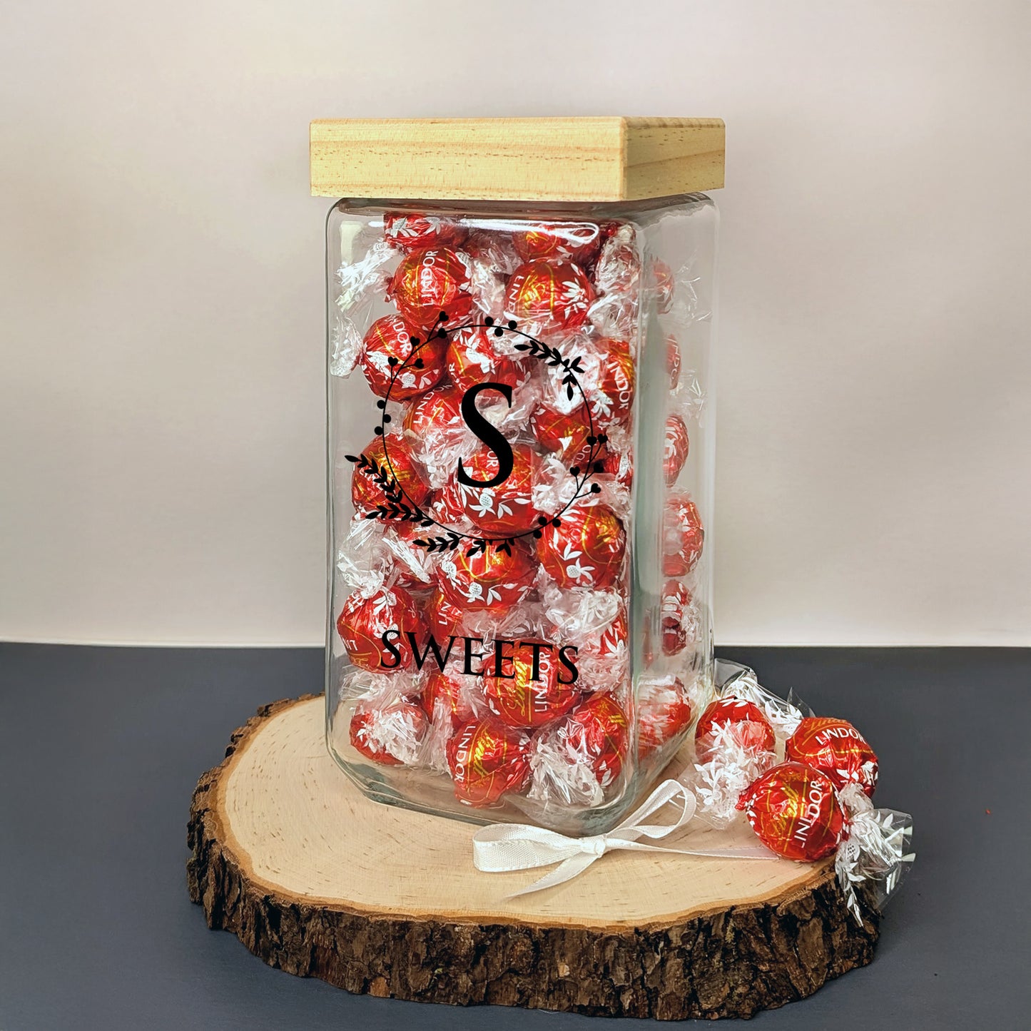 Glasdose mit Lindorkugeln und schwarzem Motiv „S“ und „SWEETS“ auf Holzscheibe