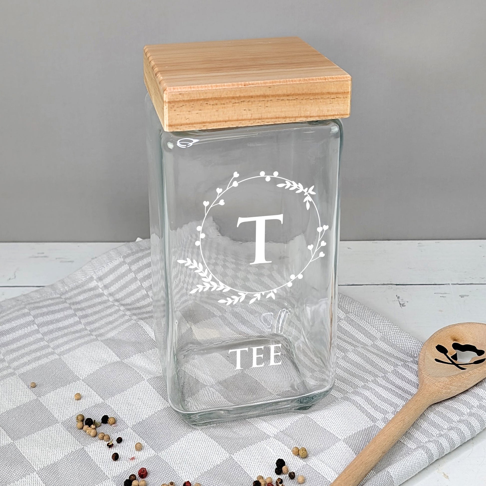Teedose aus Glas mit weißem Motiv „T“ und Schriftzug „TEE“ auf Küchentuch