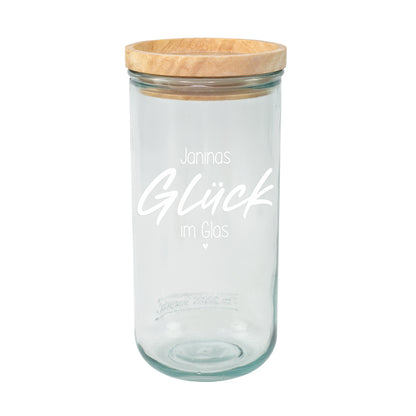 Leeres Vorratsglas mit Holzdeckel und weißem Aufdruck Janinas Glück im Glas auf hellem Hintergrund