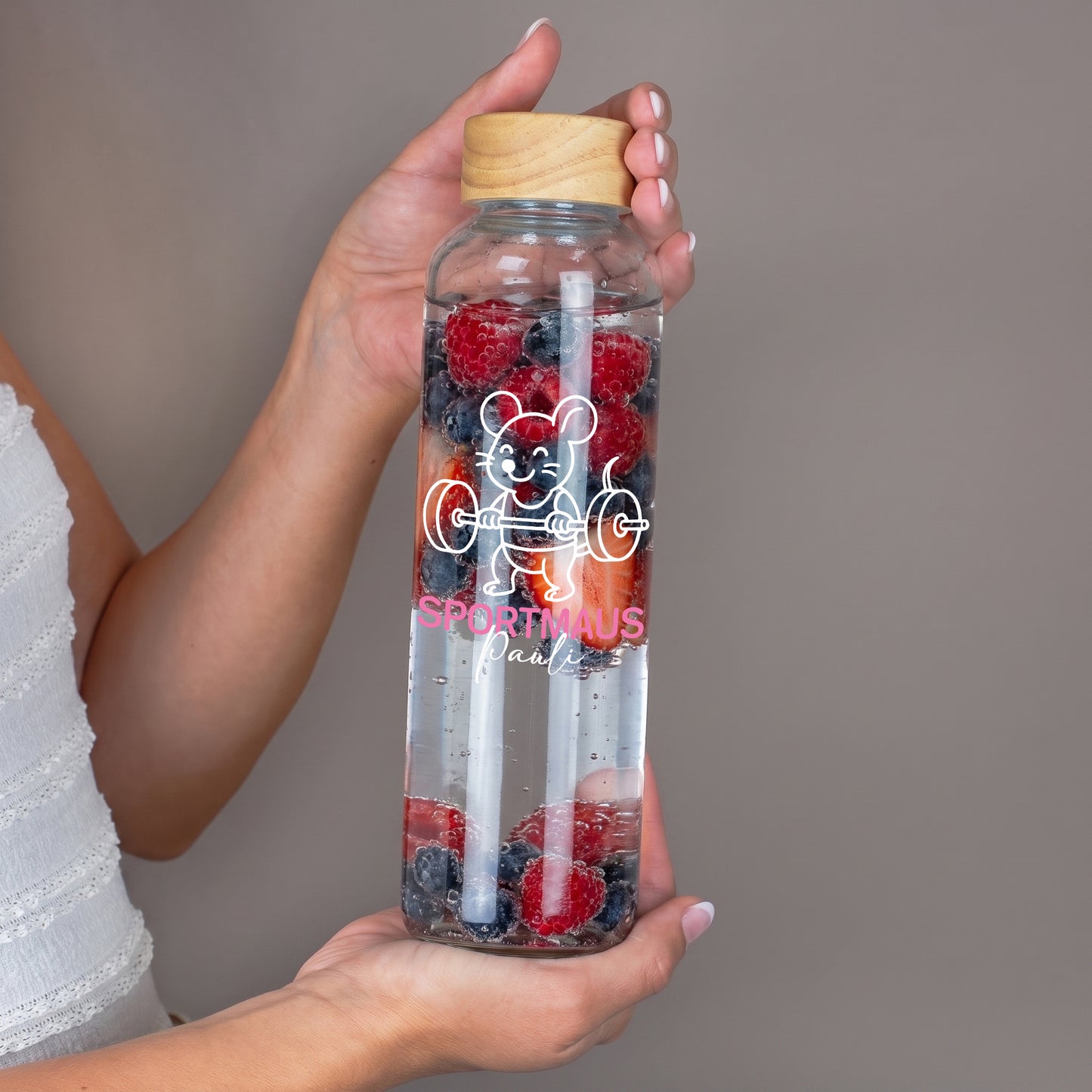 Glas Trinkflasche mit Sportmaus Motiv und Name, in Händen gehalten, gefüllt mit Beeren und Trinkhalm