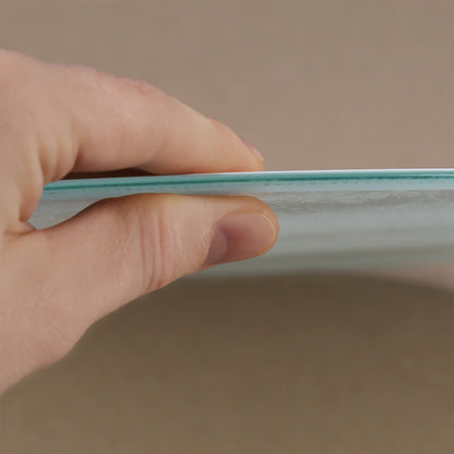 Nahaufnahme einer Hand, die das Glasbrettchen an der Kante hält. Die dünne, stabile Glasplatte ist erkennbar, ebenso wie die leicht strukturierte Oberfläche. Das Bild zeigt die hochwertige Verarbeitung und das schlanke Design des Bretts.