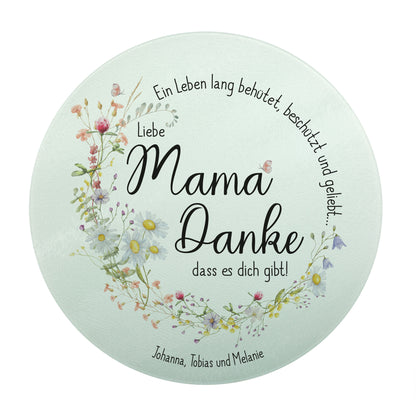 Produktbild des runden Glasbrettchens mit dem Spruch „Ein Leben lang behütet, beschützt und geliebt…“. Der Schriftzug und der zarte Wiesenblumen-Kranz bilden gemeinsam einen harmonischen Kreis. In der Mitte steht „Liebe Mama, Danke, dass es dich gibt!“. Die untere personalisierte Textzeile lautet „Johanna, Tobias und Melanie“.