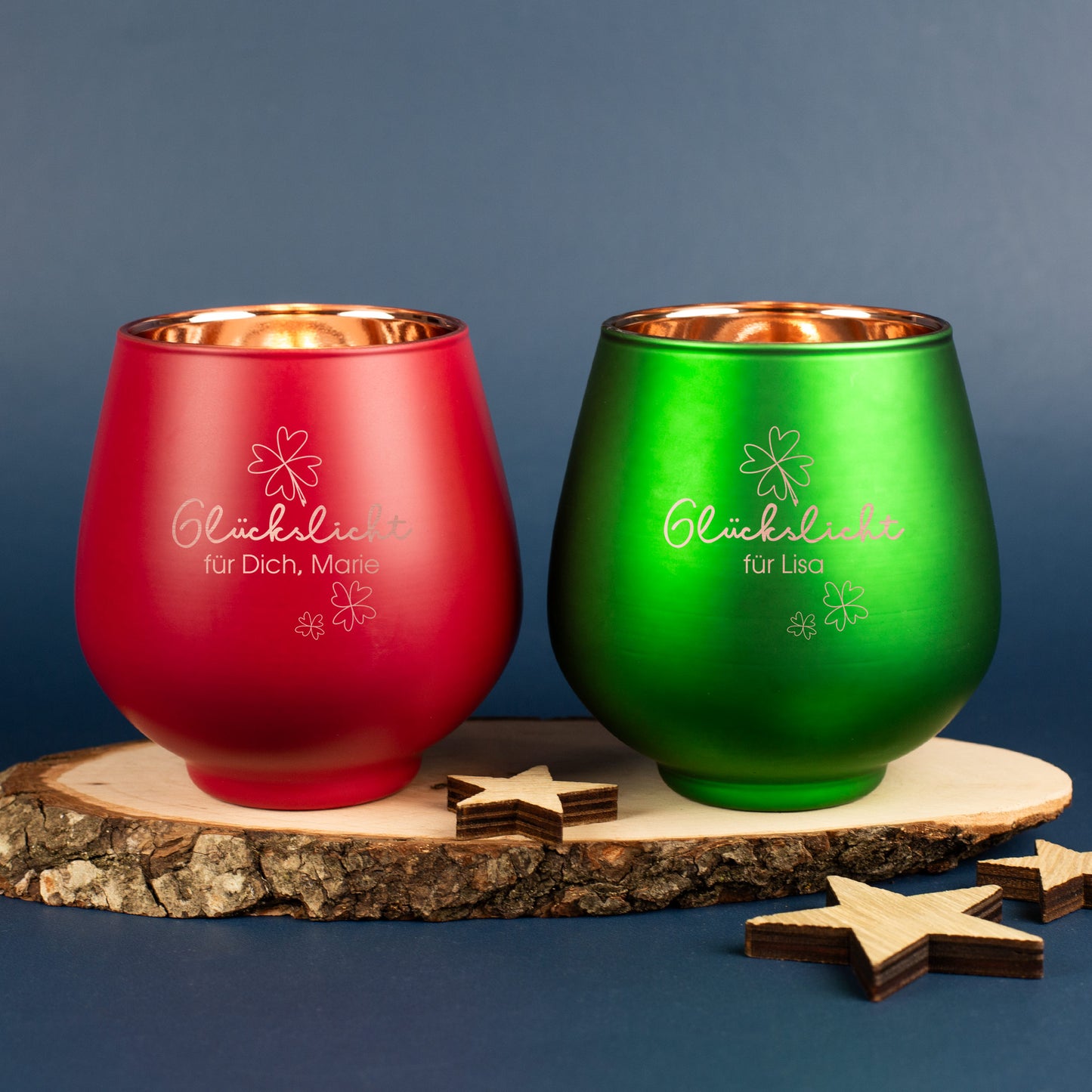 Zwei Glaswindlichter in Rot und Grün mit Gravur „Glückslicht“ und Kleeblattmotiv, auf Holzscheibe mit Sternen dekoriert