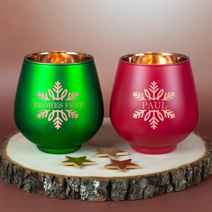Zwei Windlichter in Rot und Grün mit Schneeflockenmotiv und Gravur, dekorativ auf Holzuntergrund arrangiert