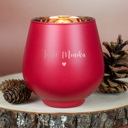 Rotes Windlicht mit Gravur „Tante Monika“ und Herzsymbol, auf Holzscheibe mit Kiefernzapfen arrangiert.