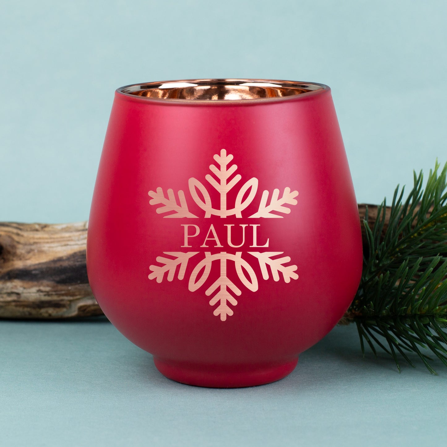 Rotes Windlicht mit gravierter Schneeflocke und dem Namen „Paul“, kupferfarbene Innenbeschichtung, weihnachtlich mit Tannenzweig dekoriert.
