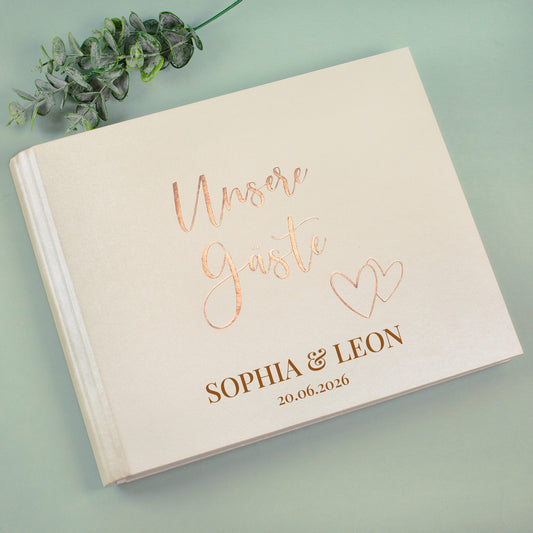 Cremefarbenes Gästebuch „Unsere Gäste“ mit Personalisierung, liegend mit Eukalyptus-Deko fotografiert.