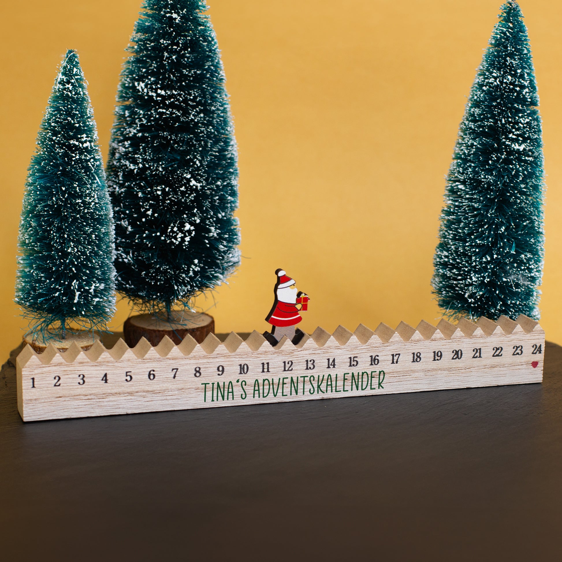 Adventskalender aus Holz mit Weihnachtsmann-Figur als Weihnachtsdeko zwischen Tannenbäumen