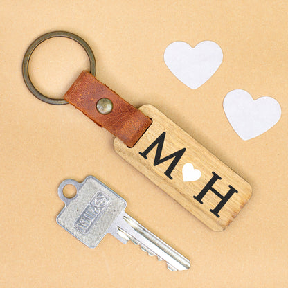 Personalisierter Schlüsselanhänger aus Holz mit Initialen M und H sowie Herz, Lederband und Schlüsselring auf hellem Untergrund