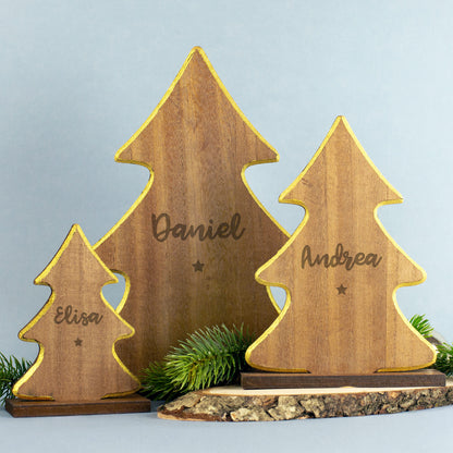 Drei weihnachtliche Holz-Tannenbäume in verschiedenen Größen mit goldfarbenem Rand und gravierten Namen „Elisa“, „Daniel“ und „Andrea“, jeweils mit kleinem Sternsymbol unter der Gravur, auf Holzsockeln stehend und mit Tannenzweig dekoriert.