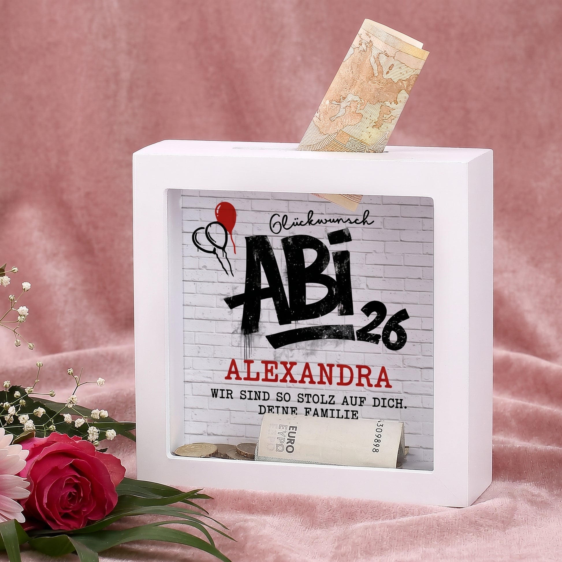 Weiße Spardose zum Abi 2026 mit Name Alexandra und Wunschtext als Geldgeschenk vor rosa Hintergrund