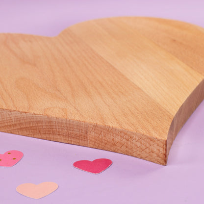 Nahaufnahme eines herzförmigen Holzbrettchens mit glatter Oberfläche und dekorativen Papierherzen im Hintergrund