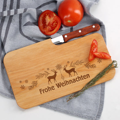 Frühstücksbrettchen aus Holz mit Gravur „Frohe Weihnachten“, dekoriert mit Tomaten und Rosmarin auf grauem Tuch