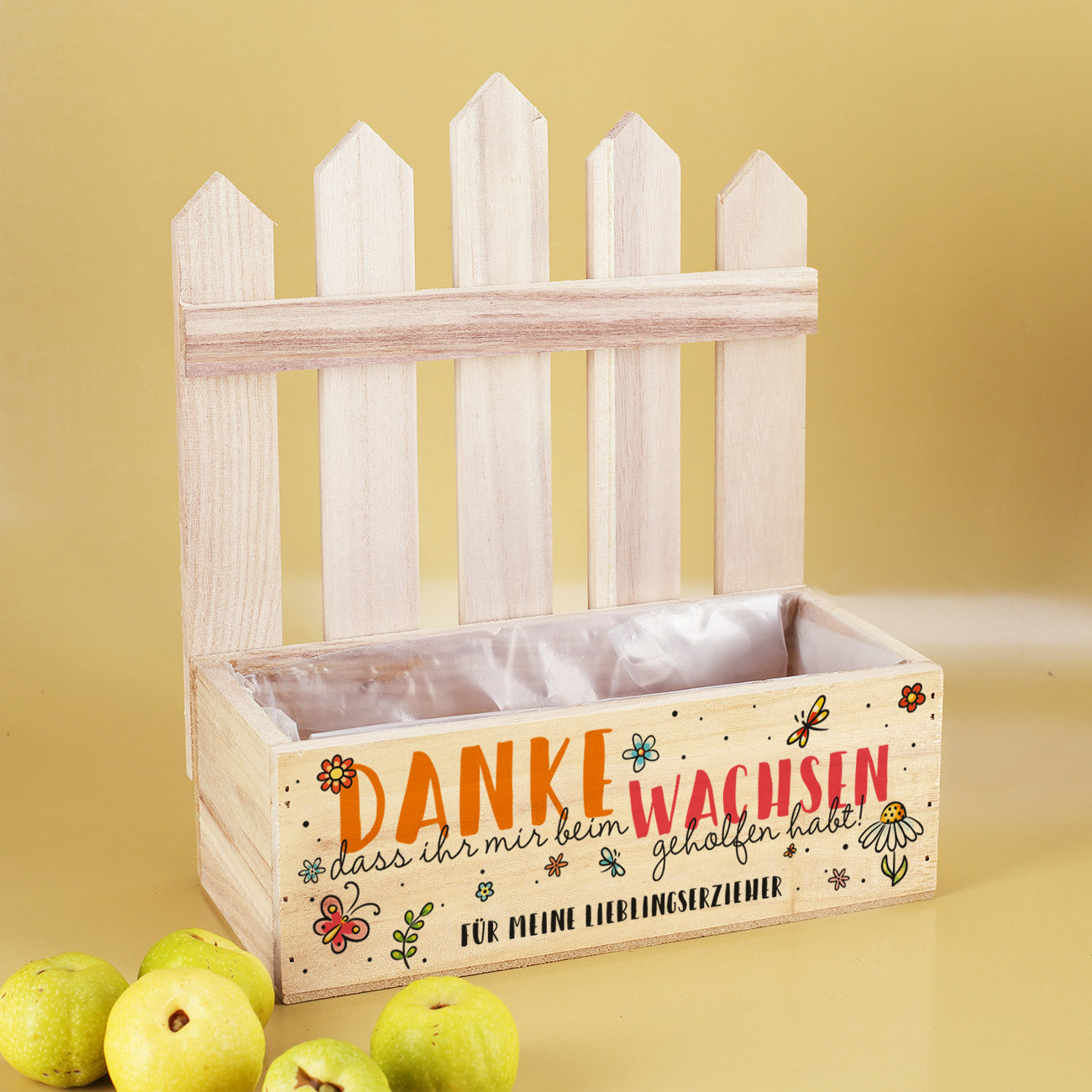 Leere Pflanzkiste mit Zaun, Aufdruck „Danke, dass ihr mir beim Wachsen geholfen habt“ und Text „Für meine Lieblings­erzieher“