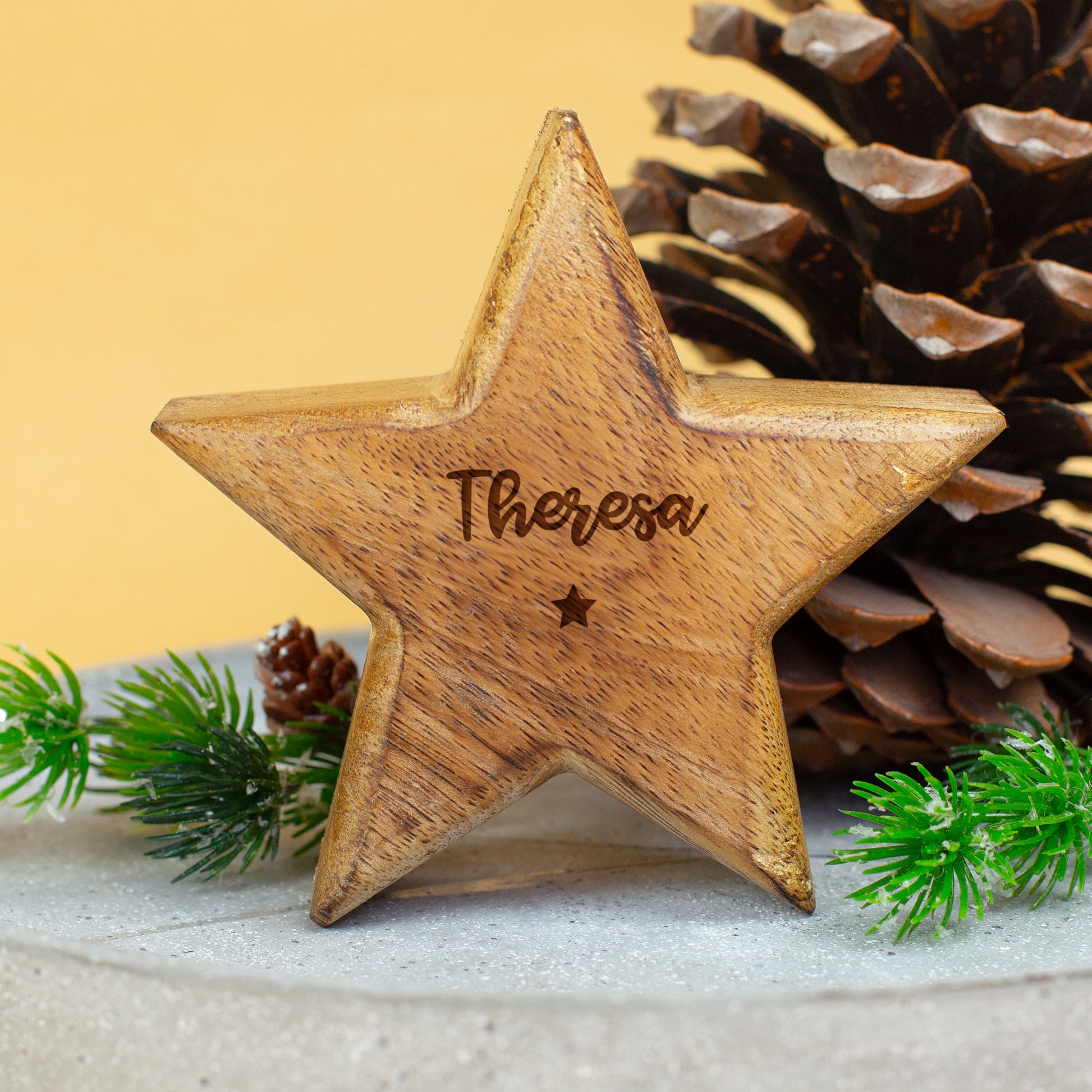 Holzstern mit Gravur „Theresa“ als dekorative Weihnachtsdeko vor Kieferzapfen und Tannenzweigen