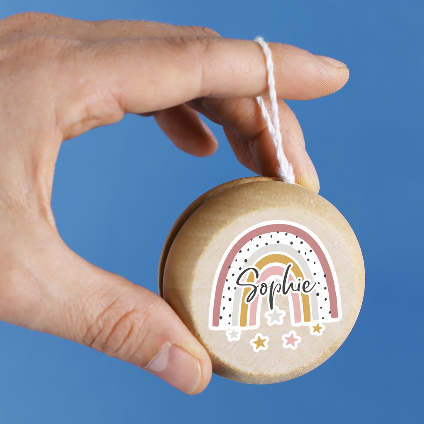 Hand hält Regenbogen-Yo-Yo mit Name Sophie vor blauem Hintergrund