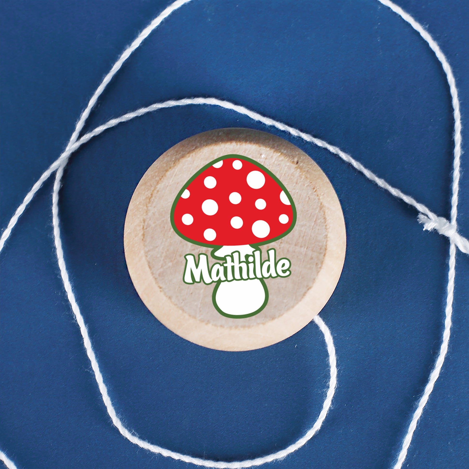 Yo-Yo mit Fliegenpilz-Motiv und Wunschname aus Holz auf blauem Hintergrund liegend