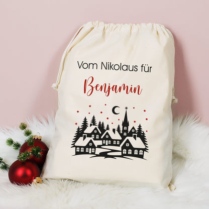 Großer Baumwoll-Geschenksack mit Aufdruck „Vom Nikolaus für Benjamin“ und Winterlandschaft, dekoriert mit Christbaumkugeln auf weißem Fell.