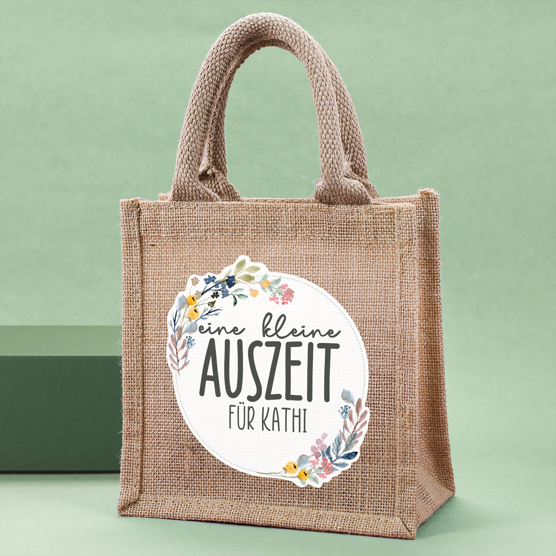 Personalisierte Geschenktasche aus Jute "eine kleine Auszeit" von der Seite vor grünem Hintergrunf