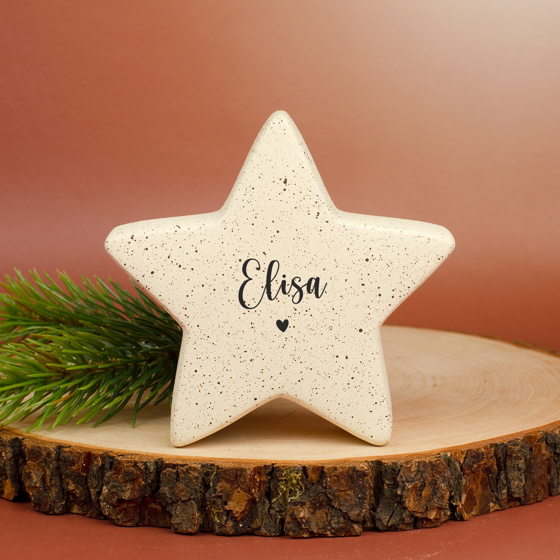 Kleiner Keramikstern in Creme mit Personalisierung „Elisa“ und Herzmotiv, dekoriert mit Tannenzweig.