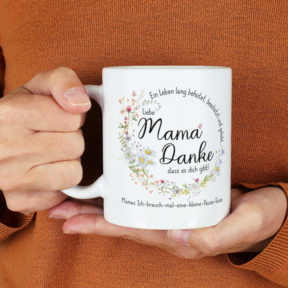 Weiße Keramiktasse mit seidenglänzendem Finish, bedruckt mit einem Wiesenblumen-Kranz und dem Spruch „Ein Leben lang behütet, beschützt und geliebt…“. In der Mitte steht „Liebe Mama, danke, dass es dich gibt!“, ergänzt durch einen individuellen Wunschtext. Die Tasse wird von einer Person in einem warmen, orangefarbenen Pullover gehalten. Ein liebevolles Geschenk für Mütter zum Muttertag, Geburtstag oder als Dankeschön.