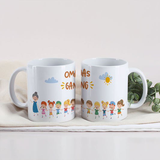 Zwei Tasse mit Motiv „Omas Gang“, Oma und eine Gruppe Kinderfiguren, auf einem weißen Tuch mit Eukalyptuszweig.