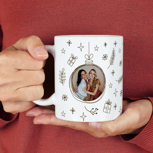 Weiße Fototasse mit Weihnachtskugel-Design in Schwarz und integriertem Foto – festlich mit Sternen und Geschenken dekoriert.