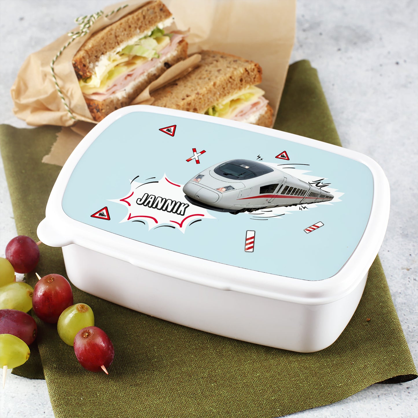 Brotdose mit ICE-Design und Name „Jannik“, daneben Pausenbrot und Obst