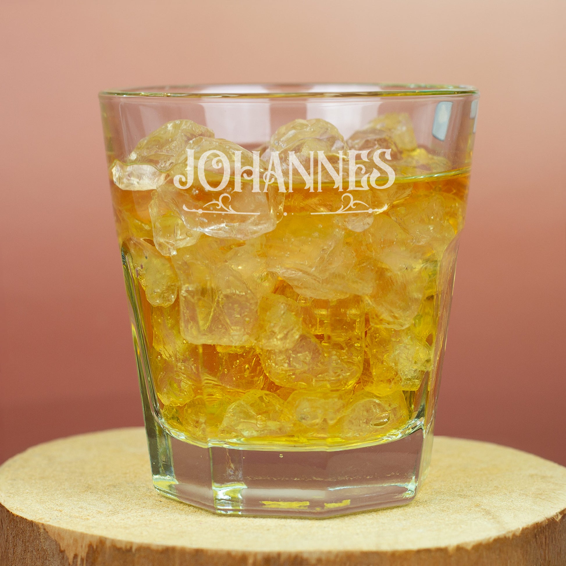 Leonardo-Trinkglas mit Gravur von Name und Ornamentmotiv, gefüllt mit Getränk und Eiswürfeln auf Holzuntergrund