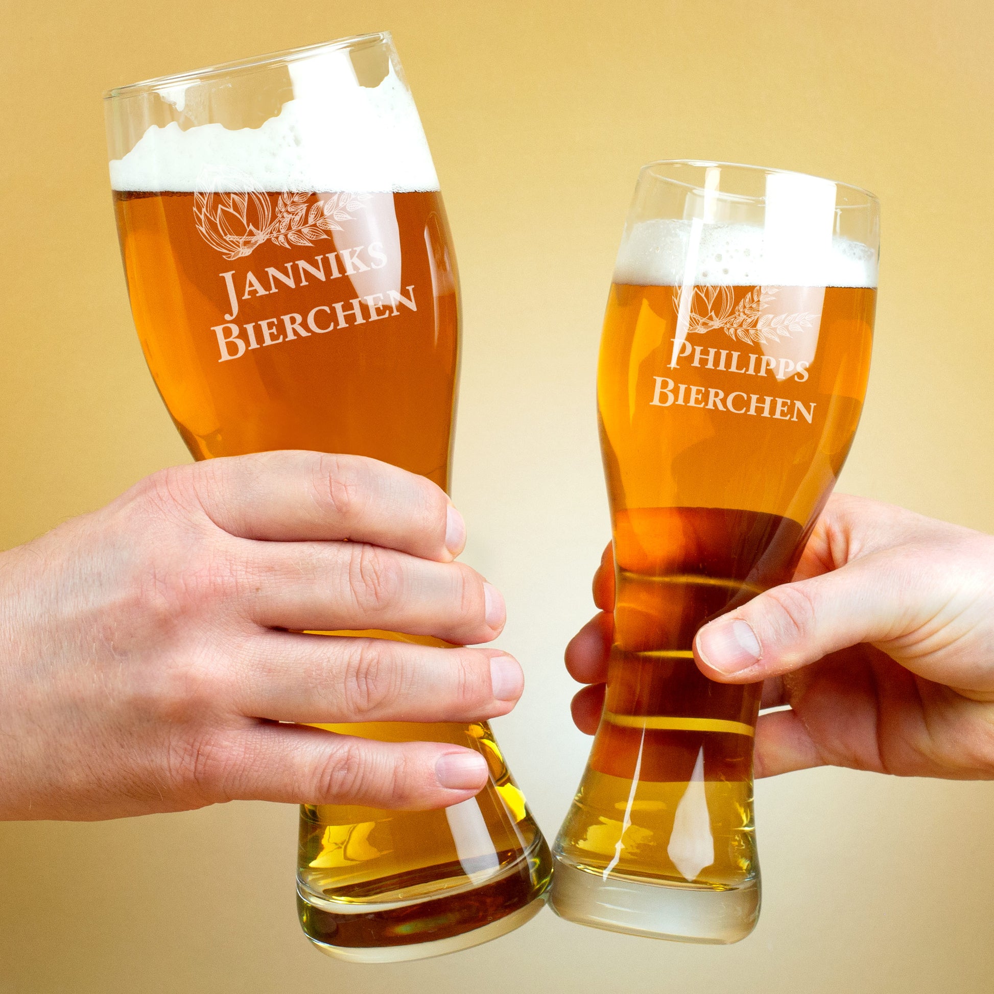 Zwei gravierte Weizengläser mit Bier, in Händen beim Anstoßen, Gravuren „Janniks Bierchen“ und „Philipps Bierchen“