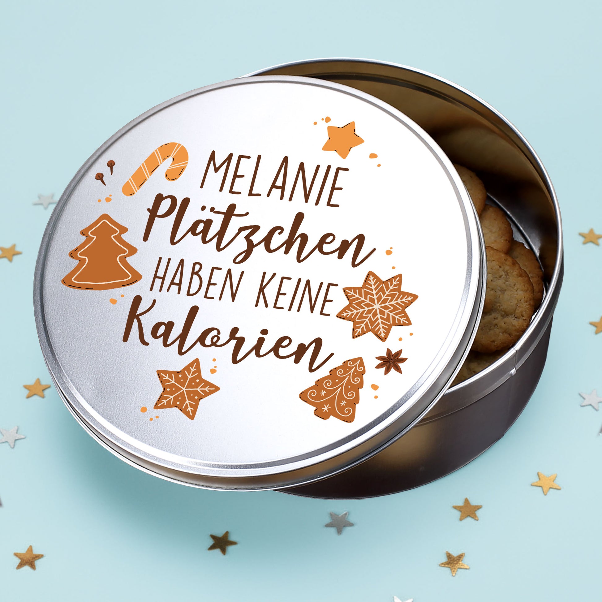 Runde Metalldose mit Spruch „Plätzchen haben keine Kalorien“ und Name Melanie, gefüllt mit Weihnachtsplätzchen auf einem hellblauen Hintergrund.