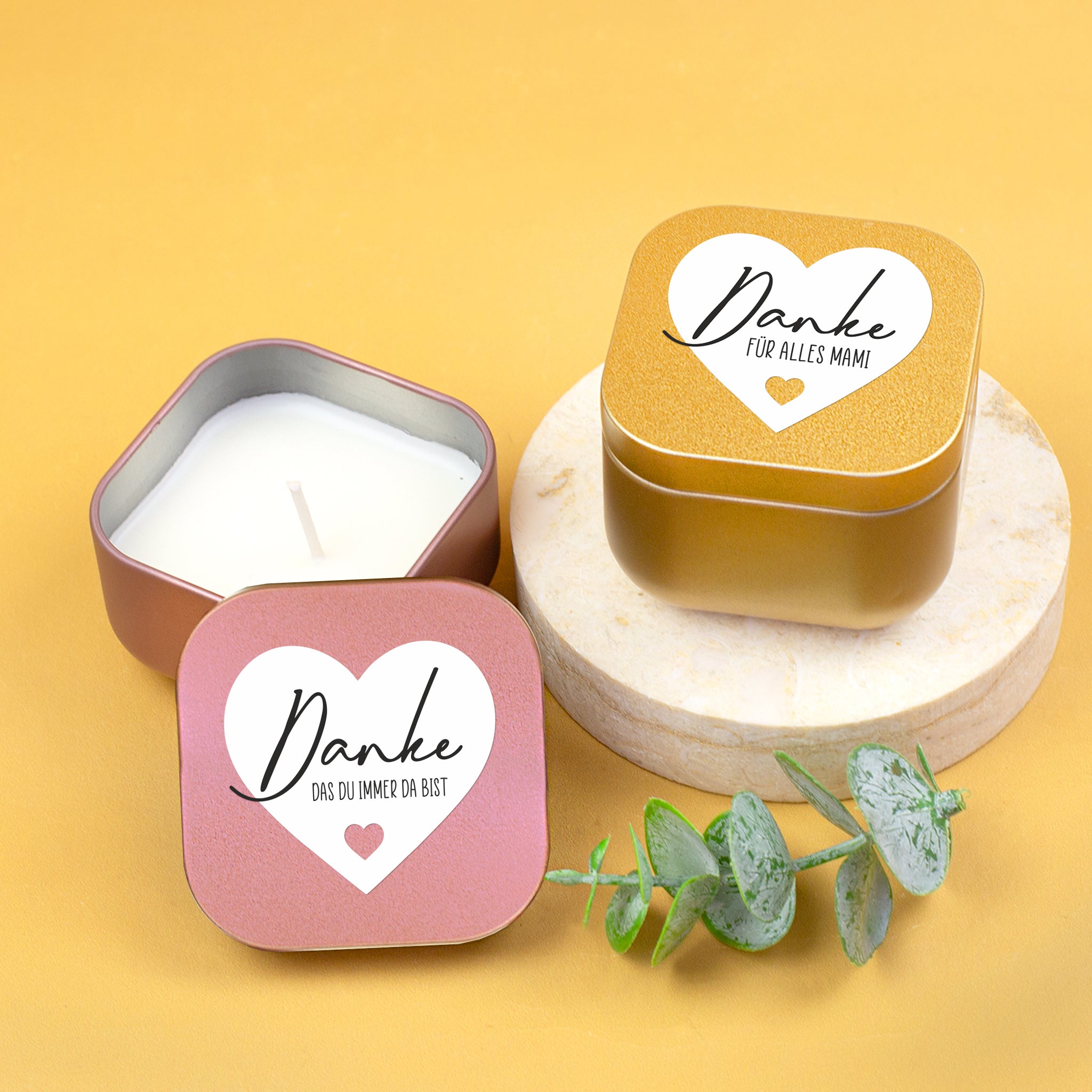 Duftkerzen in Gold und Roségold mit Herzmotiv und Danke-Schriftzug, eine Kerze geöffnet, dekoriert mit rosa Rose auf hellem Hintergrund
