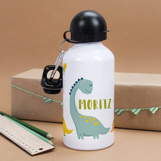 Trinkflasche mit Dino-Motiv und Name Moritz – stehend vor Geschenkverpackung, mit Bleistiften und Lineal