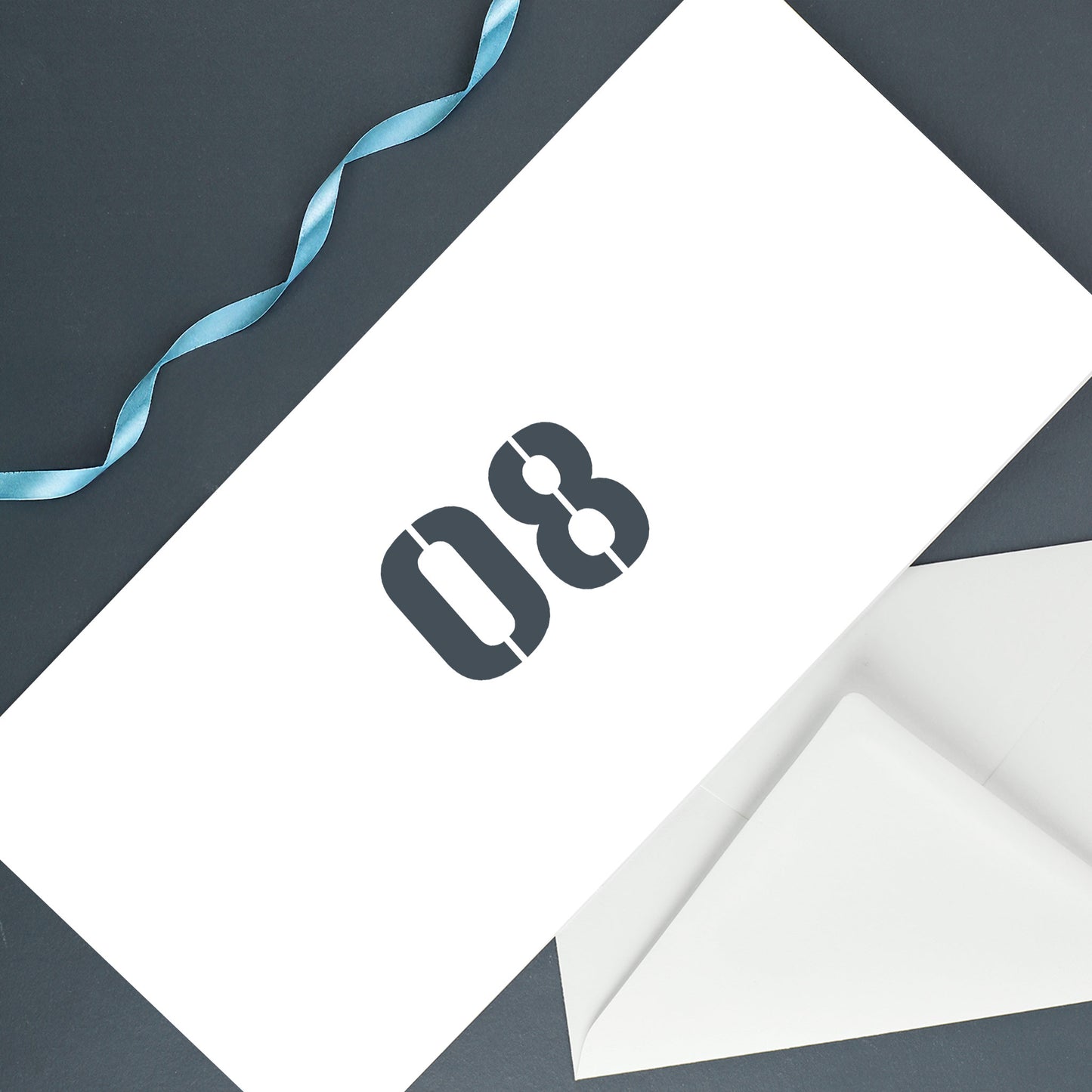 Rückseite der Geburtstagskarte mit großer grauer Ziffer „08“ auf weißem Hintergrund, daneben ein Umschlag auf dunkler Fläche mit blauer Schleife