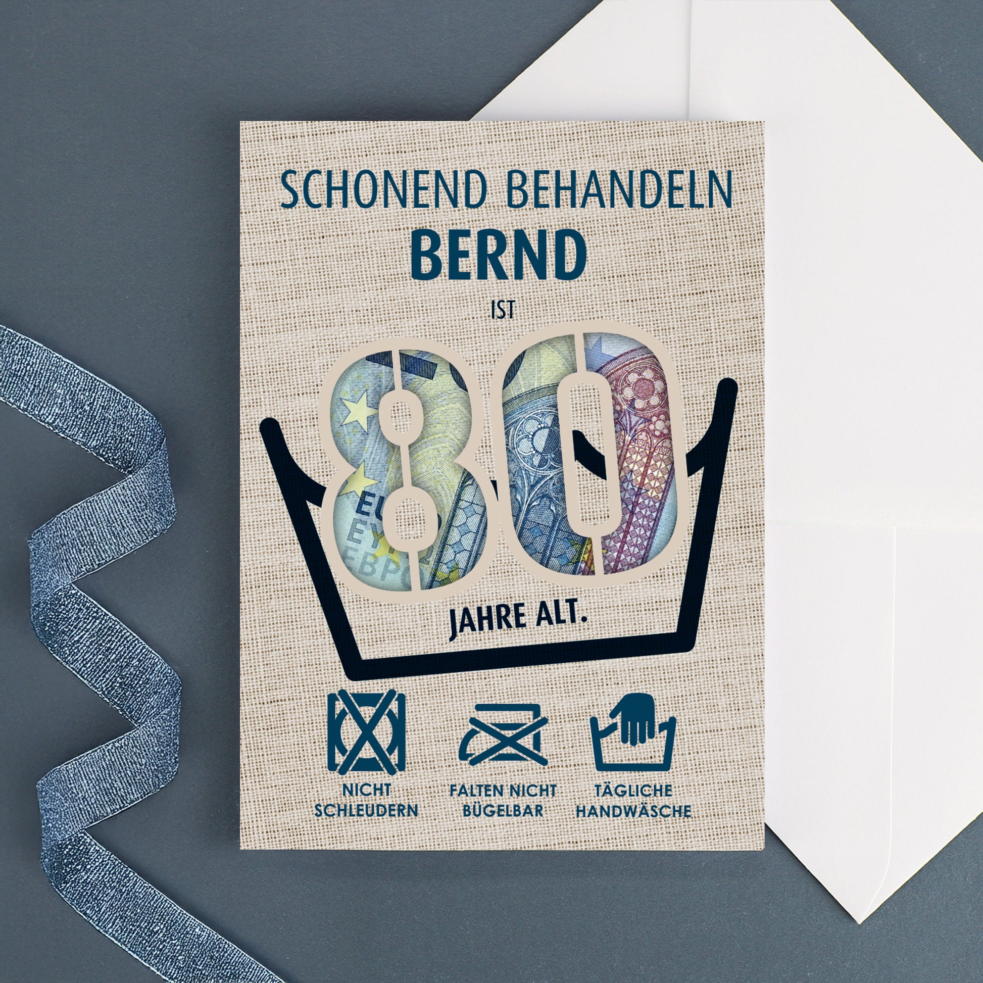 Personalisierte Geburtstagskarte mit Name „Bernd“ und sichtbarem Geldschein durch die Zahl 80, daneben ein weißer Umschlag auf dunkelblauem Hintergrund