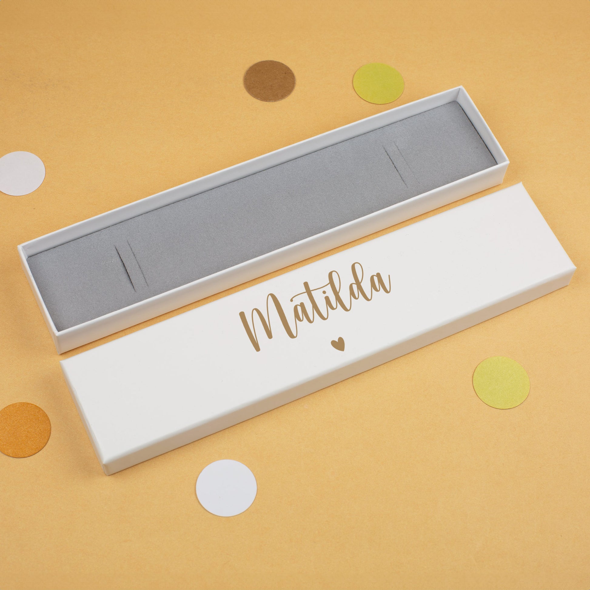 Schmuckbox in Weiß mit goldfarbenem Namen „Matilda“ und Herzsymbol, auf gelbem Hintergrund