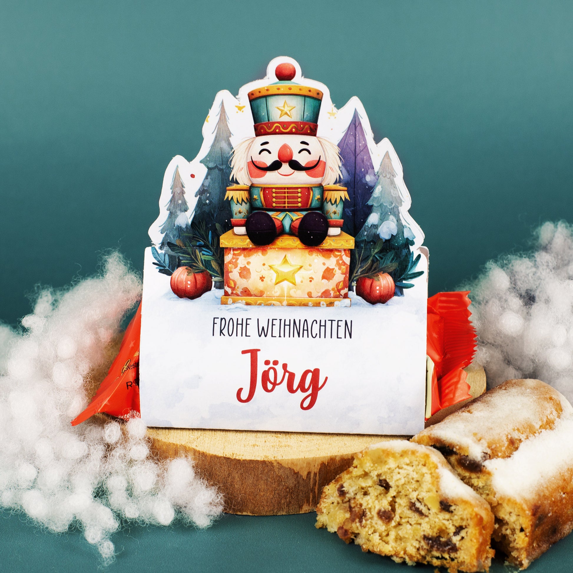 Weihnachtliche Nussknacker-Verpackung mit personalisiertem Namen „Jörg“ und Mini-Stollen, umgeben von Schneeflocken-Deko