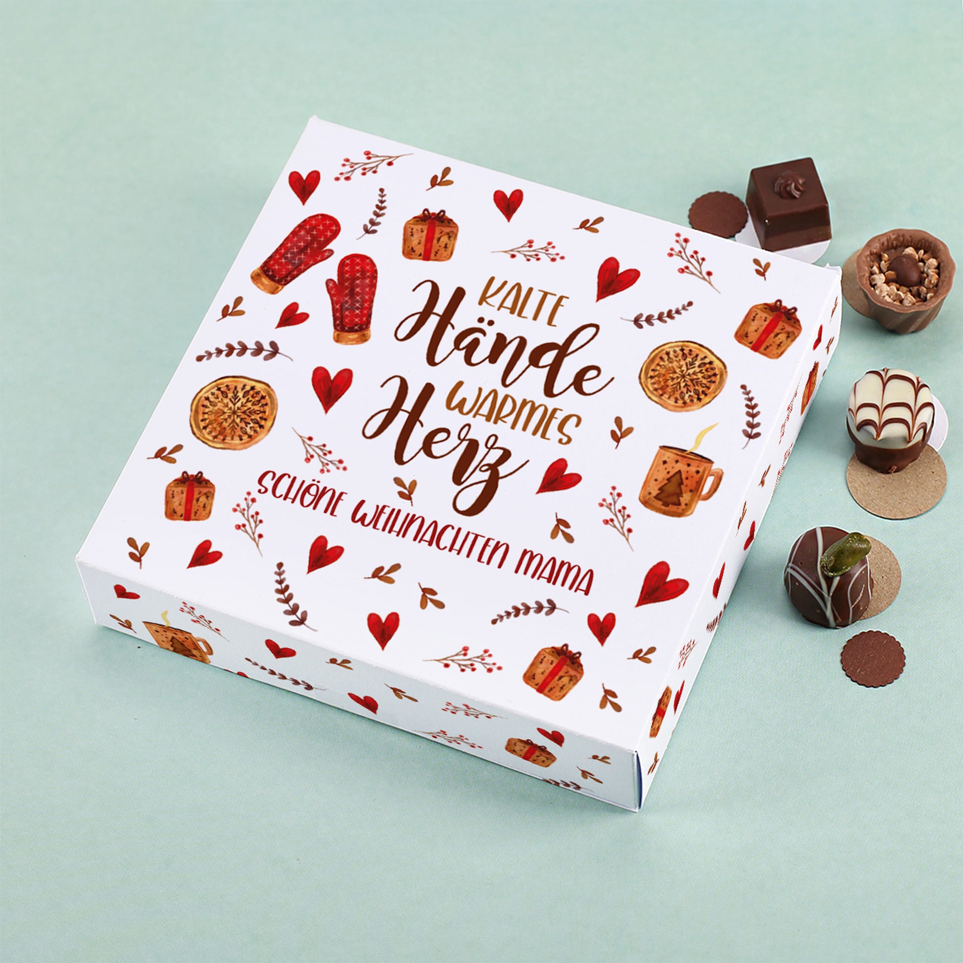 Lindt Pralinenbox mit Motiv „Kalte Hände, warmes Herz“ und personalisiertem Wunschtext „Schöne Weihnachten Mama“, umgeben von Schokolade und Pralinen auf mintgrünem Hintergrund.