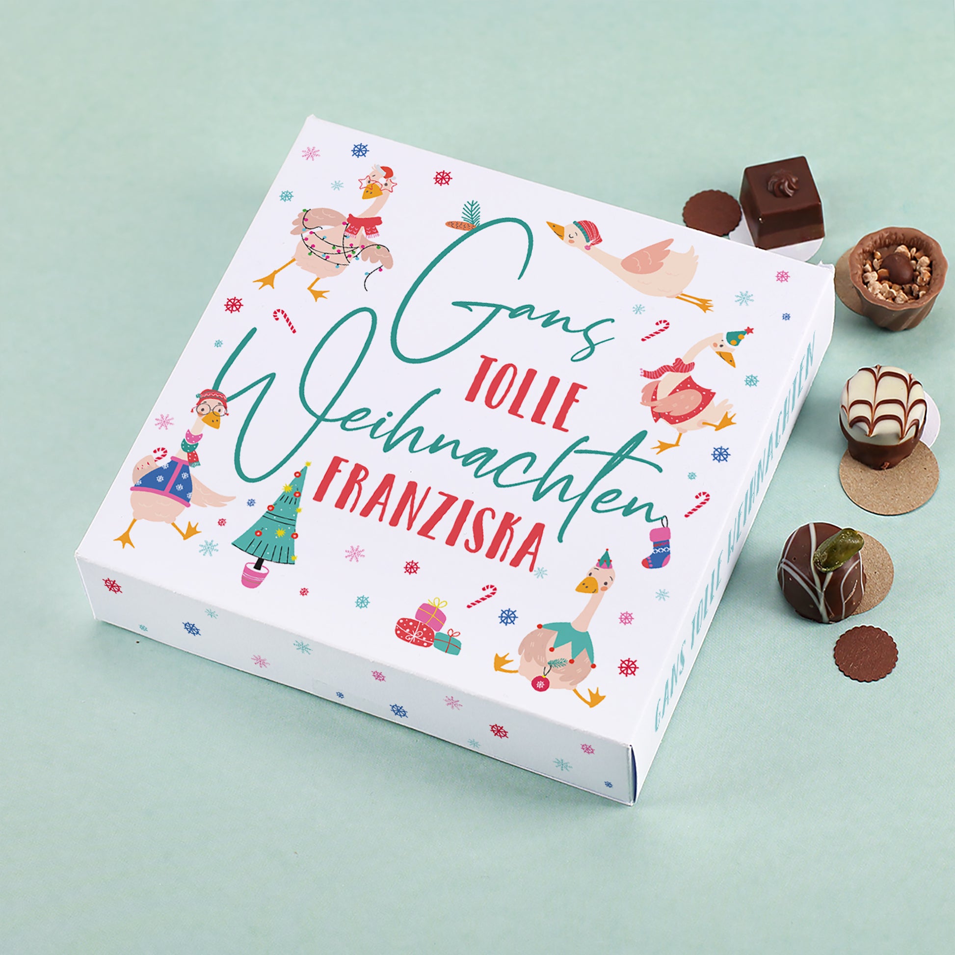 Lindt Pralinenbox mit Motiv „Gans tolle Weihnachten Franziska“, umgeben von Schokolade und Pralinen auf mintgrünem Hintergrund.