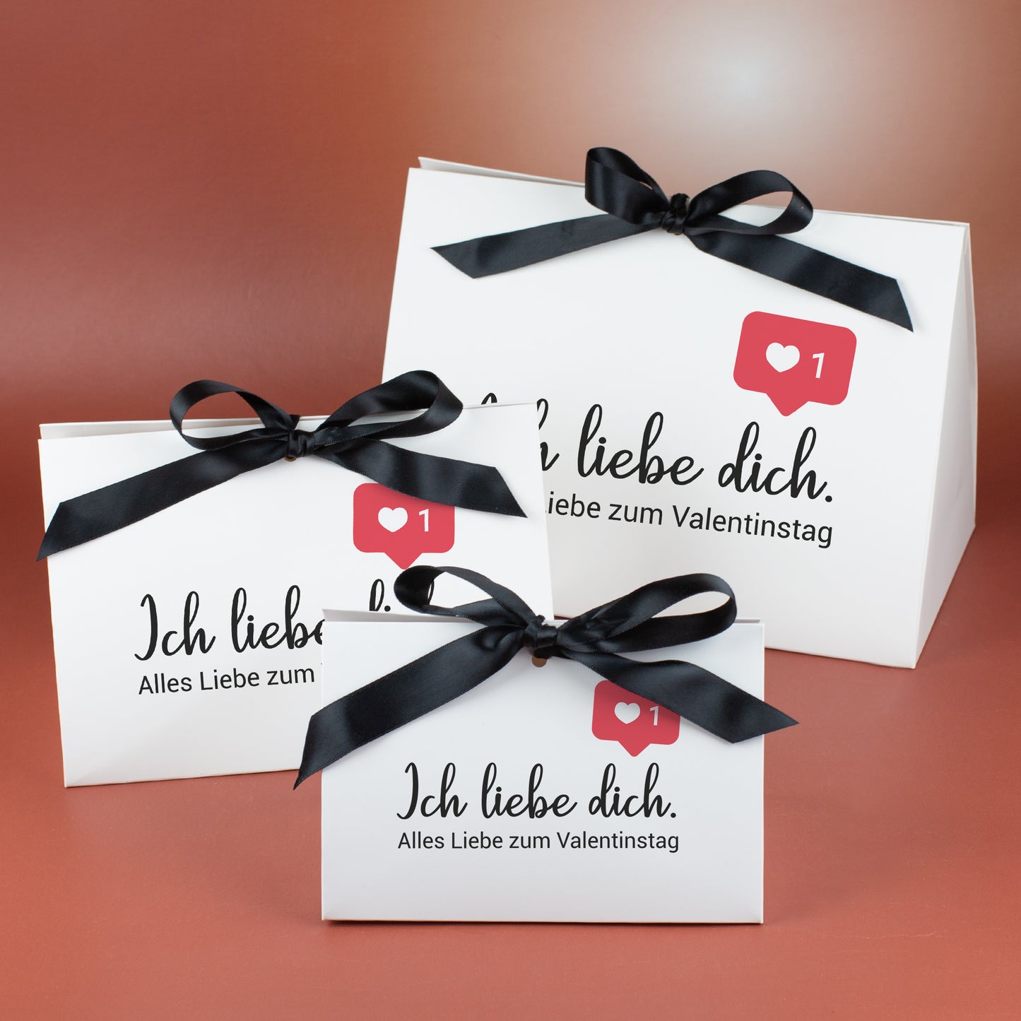 Drei weiße Geschenkverpackungen in drei Größen mit schwarzer Satinschleife und Aufdruck „Ich liebe dich“ mit Valentinstagsgruß