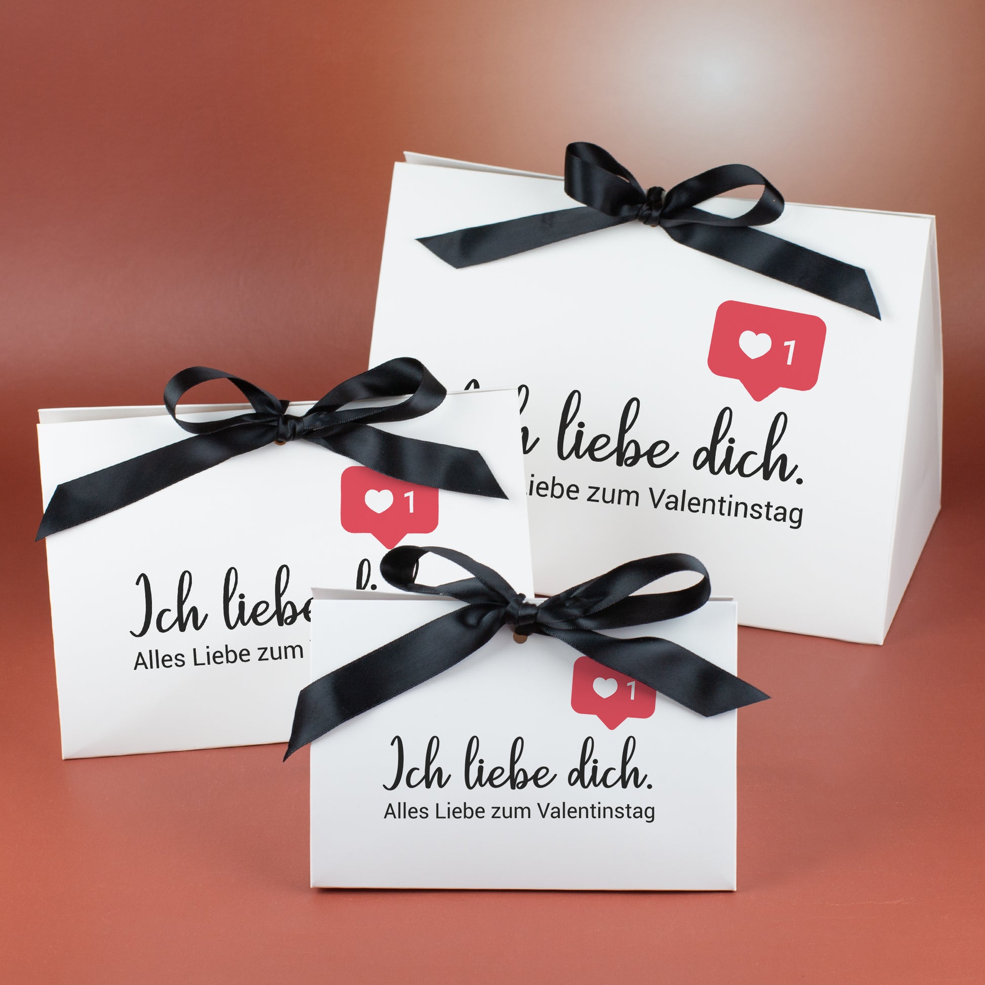 Drei weiße Geschenkverpackungen in drei Größen mit schwarzer Satinschleife und Aufdruck „Ich liebe dich“ mit Valentinstagsgruß
